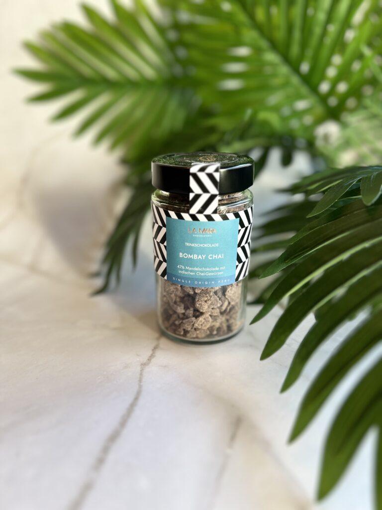 Glasbehälter mit Trinkschokolade Bombay Chai und grünen Pflanzen im Hintergrund