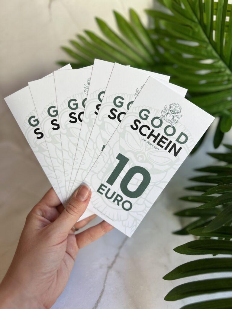 Hand hält mehrere Good Schein Gutscheine im Wert von 10 Euro