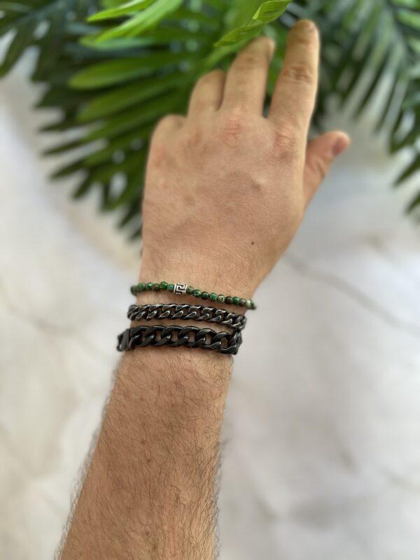 Hand mit mehreren Armreifen vor einem grünen Blatt.