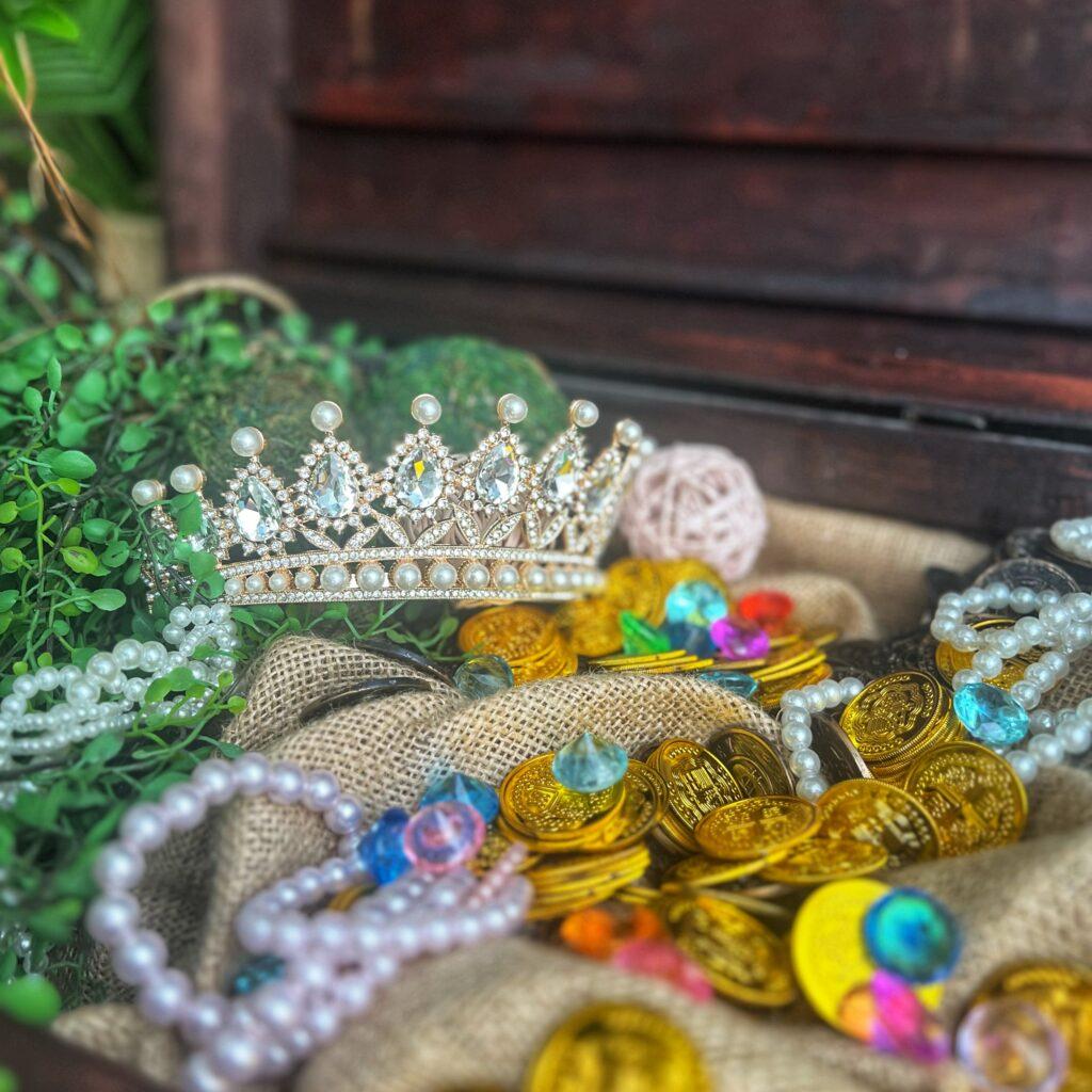 Kulinarische Erlebnisreise! Eine glänzende Krone auf einem Haufen von Goldmünzen und Schmuck, umgeben von grünem Blattwerk