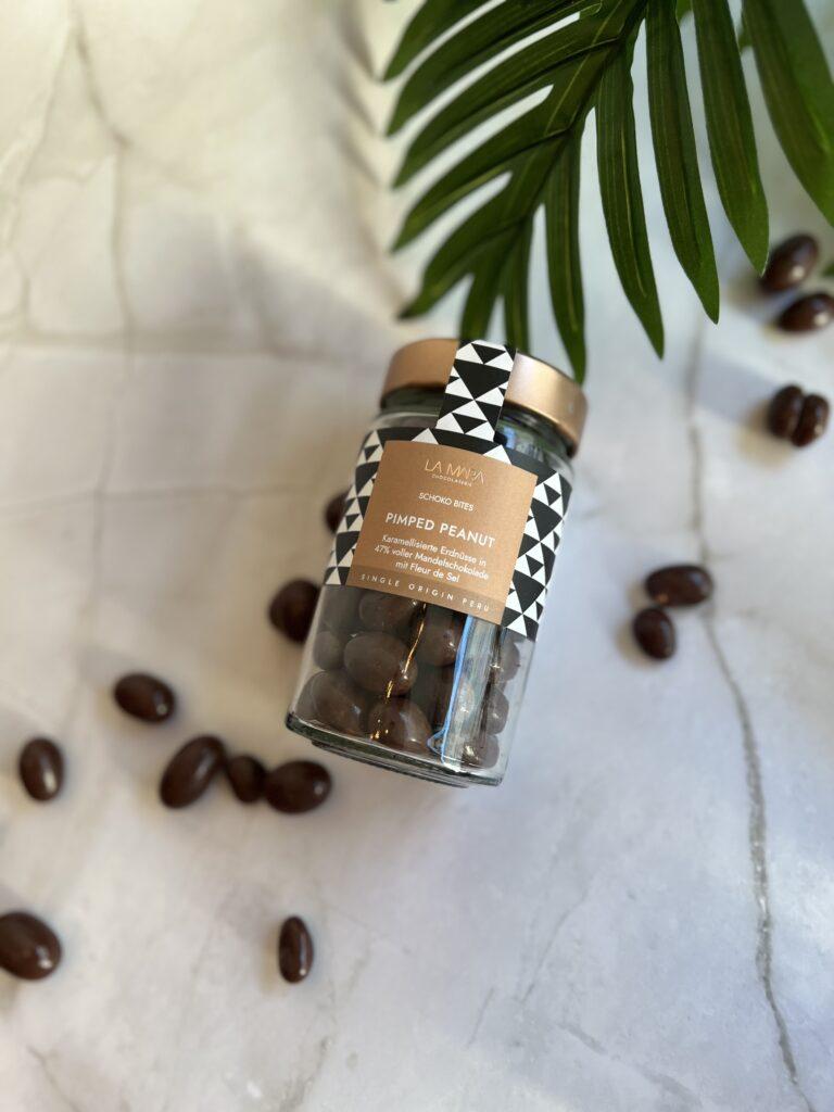 Glas mit karamellisierten Erdnüssen in Schokolade auf Marmortisch