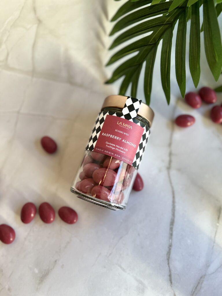 Glasbehälter mit Himbeer-Mandel-Schoko-Bissen von La Mara auf einem Marmortisch