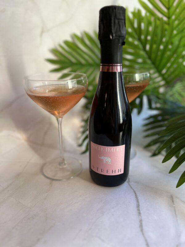 Flasche Shiki Miki von Strehn und ein Glas mit rosé Sekt vor grünen Pflanzen