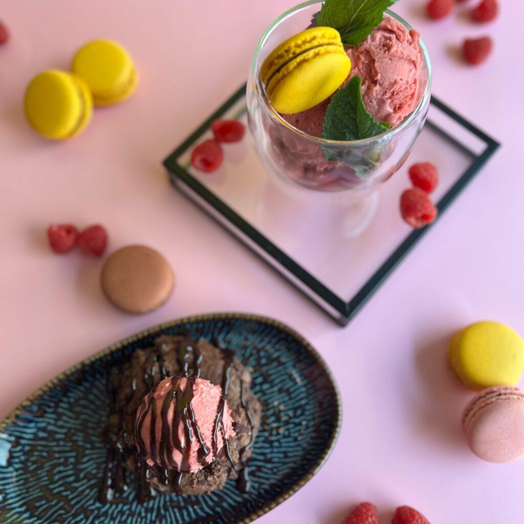 Eine stilvolle Dessertpräsentation mit Himbeersorbet, gelben und rosa Macarons sowie frischen Himbeeren.