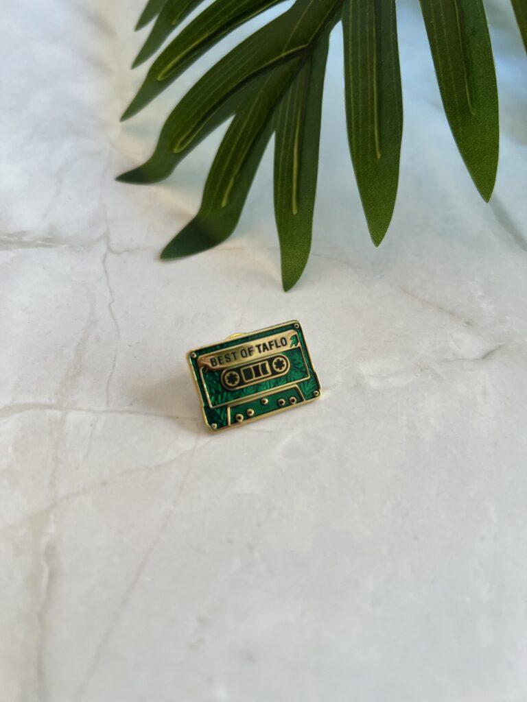 Bunte Retro-Kassetten-Pin auf einem weißen Marmortisch mit Pflanzenblatt