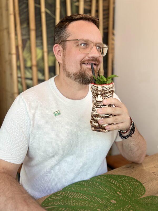 Mann mit einem exotischen Cocktail aus einem Tiki-Becher und frischer Minze an einem Holztisch
