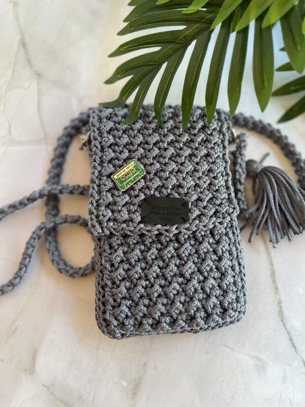 Stylische graue Handtasche mit einer Quaste und einem grünen Taflo Pin