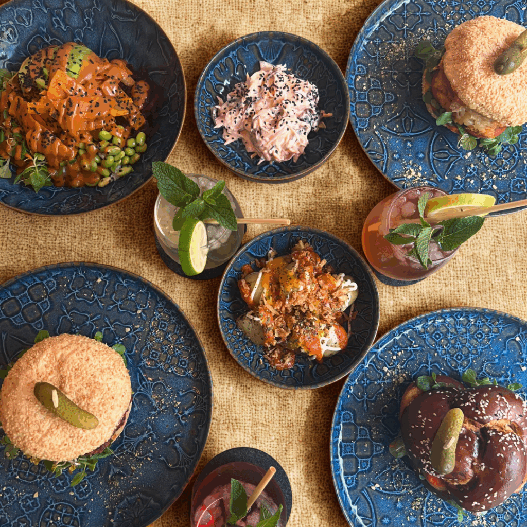 Food Adventure: Vielfältige Gerichte auf blauen Tellern, darunter Burger, Bowls und Getränke